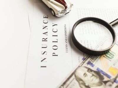 Insurance policy forms with a toy car, magnifying glass, and a one hundred dollar bill.