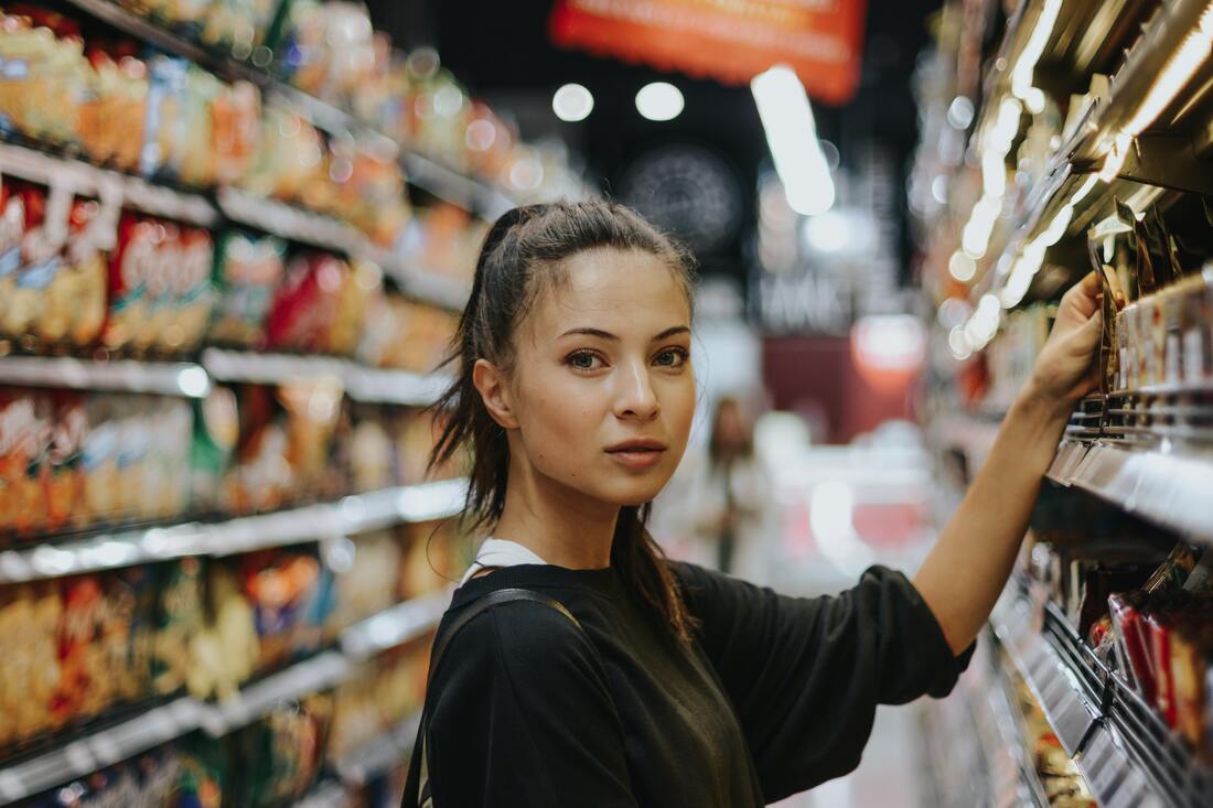 A young woman with a ponytail and baggy black sweater reaches for an item on a grocery shelf in Halifax.