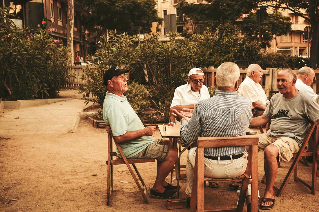 Men with hearing aids sit outside around a table and play a game at Northumberland Senior Action Center.