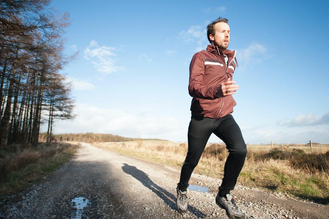 man-in-tracksuit-with-hearing-aids-jogs-outdoors-on-gravel-road-along-field-in-sunbury