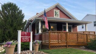 northumberland-hearing-center-advertised-sign-in-front-of-red-house-with-brown-wooden-porch-and-american-flag
