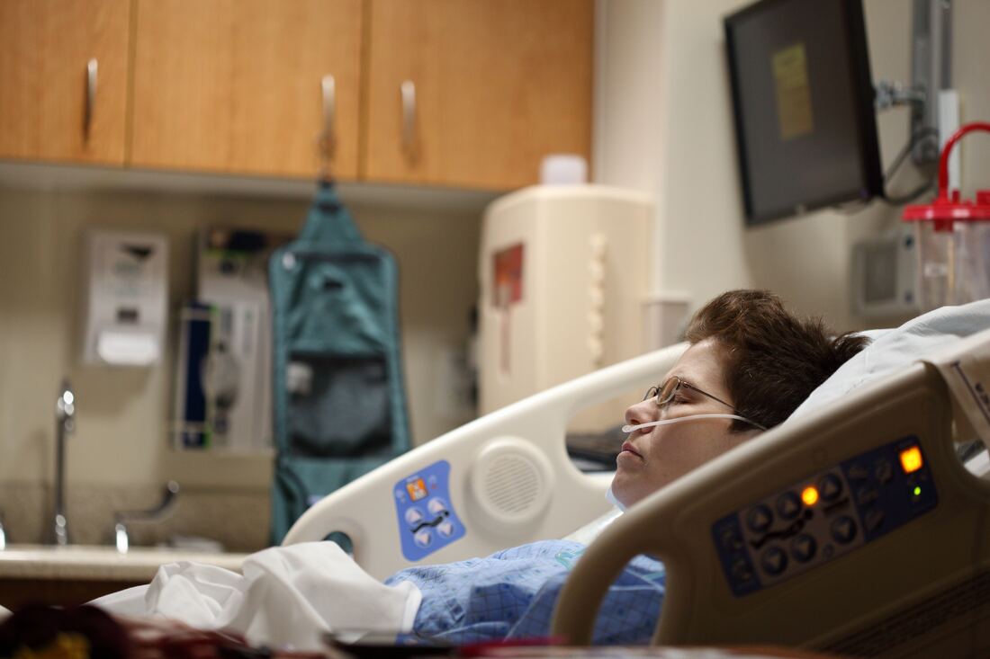 A patient with hearing loss rests on a hospital bed.